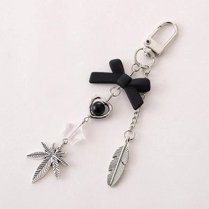 Detail of cross keychain with black bow, heart charm, and metallic feather pendant