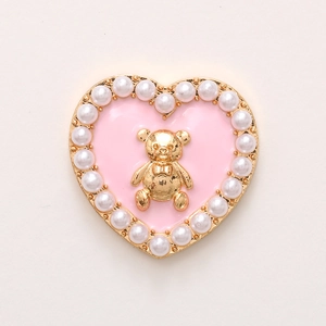 Detailed macro view of heart-shaped charm with pink enamel, golden bear, and pearls