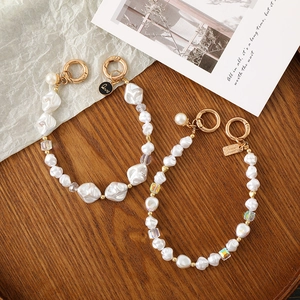 Detailed macro of baroque pearl phone charms with gold clasps and love tags on dark wood