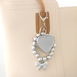 Detailed close-up of a silver heart frame pendant with bow and bead chain on a bag