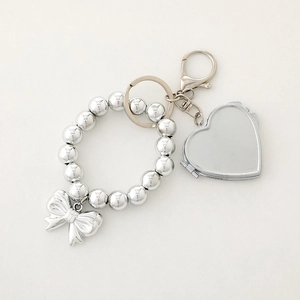 Silver beaded keychain featuring a metallic heart-shaped locket and a bow pendant