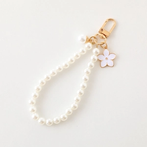 Detail of white pearl phone charm with a gold metal clasp and enamel flower pendant