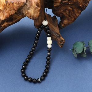 Detail of beaded phone strap with black agate and white jade beads on decorative wood