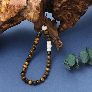 Detail of tiger eye bead phone strap with white accents on rustic wooden decor