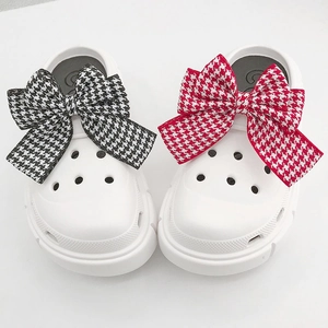 Detail of white clogs featuring oversized houndstooth bow charms and airy vents