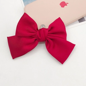 Detailed close-up of a vibrant red satin bow shoe accessory with a silver metal spring clip