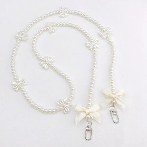 Detail of cream white pearl phone strap featuring elegant resin bows and silver lobster clasps