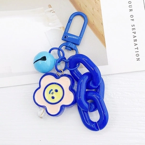 Détail d'un porte-clés fleur bleue avec visage souriant, chaîne en plastique et clochette