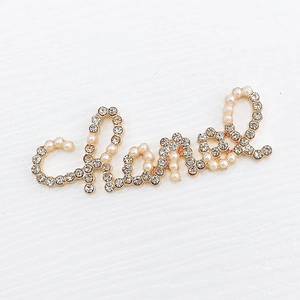 Detailed close-up of golden letter charm with inlaid pearls and sparkling crystals