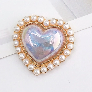 Macro detail of heart-shaped iridescent gem charm with white pearl border and gold base