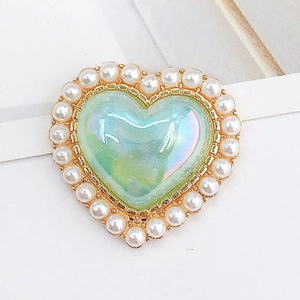 Detail of heart-shaped charm with iridescent green center, pearls, and gold base