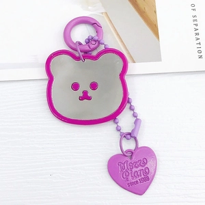 Détail d'un porte-clés miroir ours violet avec étiquette cœur sur fond texturé blanc