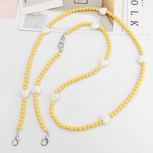 Macro detail of yellow beaded chain featuring white hearts and silver lobster clasps