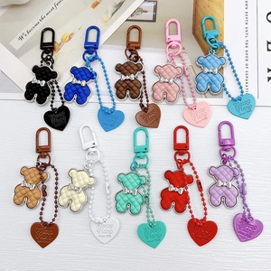 Colorful checkered bear keychains with silver bow ties and heart tags on white wood