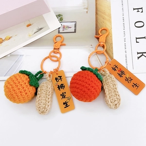 Detail of crochet persimmon and peanut keychain with Good Luck charm on white surface