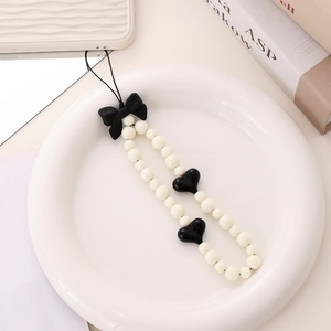 Acrylic beaded phone strap with black ribbon bow and heart charms on a white ceramic plate