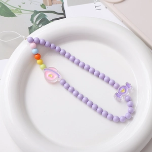 Detail of beaded phone strap with acrylic planet and candy charms on white plate