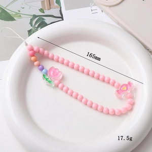 Pink beaded phone wrist strap with floral tulip and candy charms on white ceramic plate