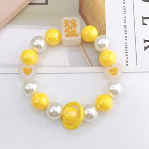 Détail de la dragonne en perles jaunes avec breloque mah-jong sur un bureau blanc