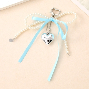 Llavero de lazo de perlas con cinta azul claro y colgante de corazón plateado sobre fondo beige
