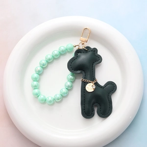 Détail du porte-clés girafe en cuir vert foncé avec perles irisées et médaille Lucky