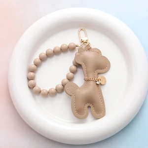 Détail d'un porte-clés girafe en cuir beige avec dragonne perlée sur un plateau blanc