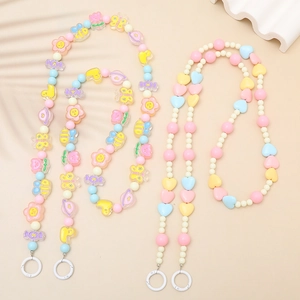 Pastel acrylic beaded phone lanyard with candy hearts and bee charms on a beige table