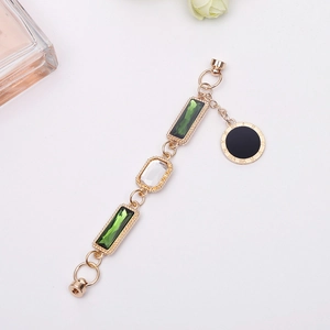 Golden bracelet with green gems and Roman numeral pendant on a minimalist background