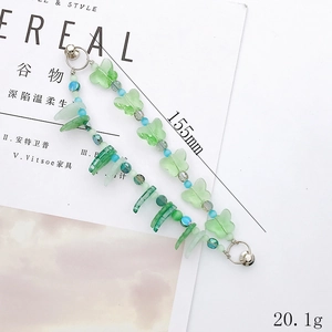Green butterfly beaded phone charm with dual silver metal hooks on a magazine background