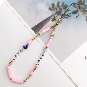 Detail of pink clay beads, golden spacers, and Evil Eye charms on a boho phone strap