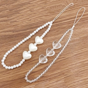 Beaded phone charms featuring white pearls and clear acrylic hearts on wooden background