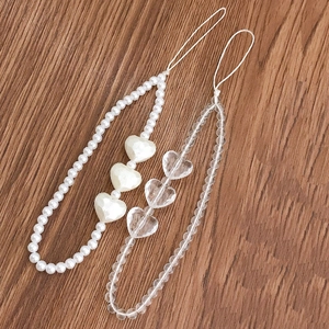 Elegant pearl and clear heart beaded phone wrist strap charms on a wooden surface