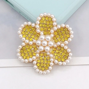 Primer plano de dije floral con pedrería amarilla y perlas en pétalos de forma hexagonal