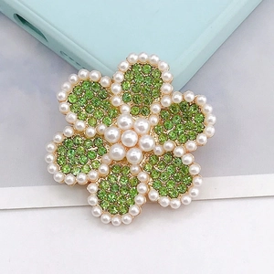 Detalle del broche de flor de aleación con strass verde y perlas blancas en base oro
