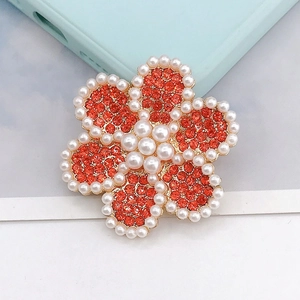 Detalle de dije de flor con diamantes naranjas y perlas blancas sobre base dorada