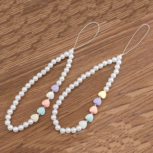 Détail de dragonnes de téléphone en perles avec cœurs macaron sur fond de bois brun