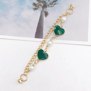 Detail of double-layer gold bracelet with green heart charms and white pearls on white background