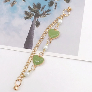 Detail of gold chain bracelet featuring green heart charms and elegant white pearls