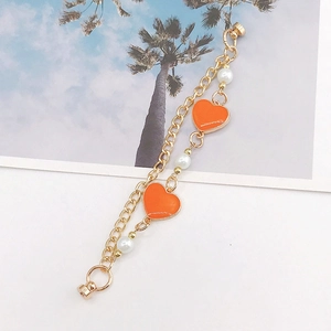 Detail of a double-layered gold chain with orange enamel hearts and white pearls