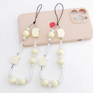Detail of beaded phone charms with pearlescent beads and pumpkin accents on pink case