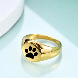 Detailed view of a gold signet ring featuring a black paw print on a round polished surface