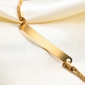 Macro detail of a 6mm gold-plated stainless steel ID bar bracelet with a twisted rope chain