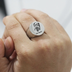 Close-up of a silver signet ring featuring a skull engraving and I'M OKAY text detail