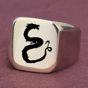 Dettaglio macro dell'anello a sigillo dorato quadrato con motivo a drago nero inciso