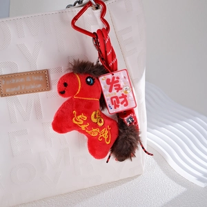 Red plush horse keychain with gold embroidery and acrylic lucky tags on a white quilted bag