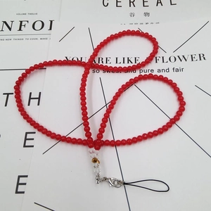 Detail of red beaded phone lanyard with golden charms and silver lobster clasp on a magazine