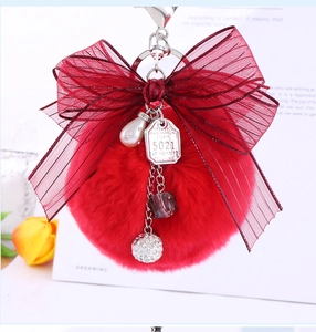 Close-up of red faux fur pompom keychain with organza bow and pearl charm accents