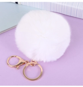 Détail d'un pompon blanc en fausse fourrure avec un fermoir mousqueton en métal doré rose
