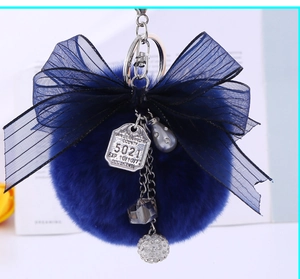 Detail of navy blue faux rabbit fur pompom keychain with a black mesh ribbon and silver charms