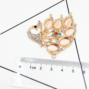 Macro shot of gold peacock pendant with cat eye stones and rhinestones showing 5.5cm size